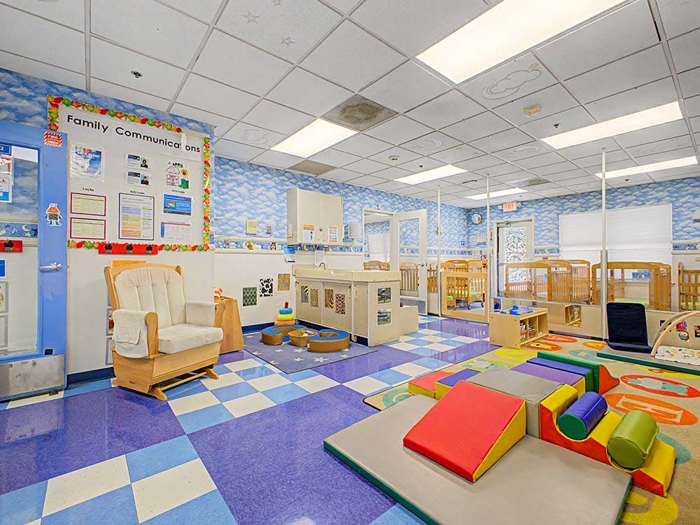 childcare room with cribs, play mats, and a rocking chair