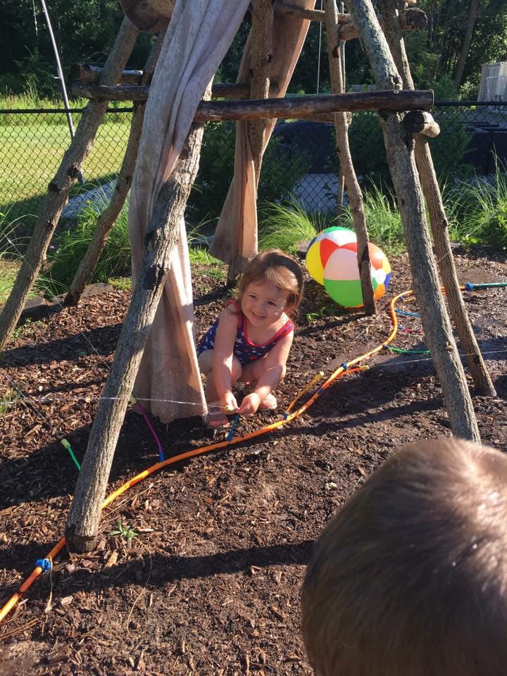 Child crouching under a wooden structure with a beach ball nearby