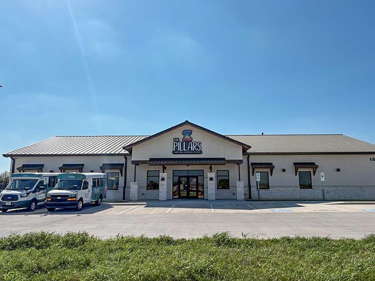 Exterior of The Pillars learning center building with two vans parked in the parking lot