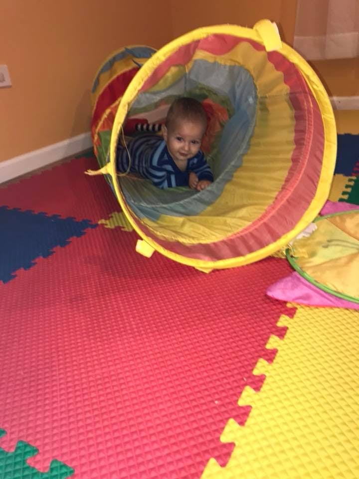 Child crawling through a play tunnel on a colorful mat
