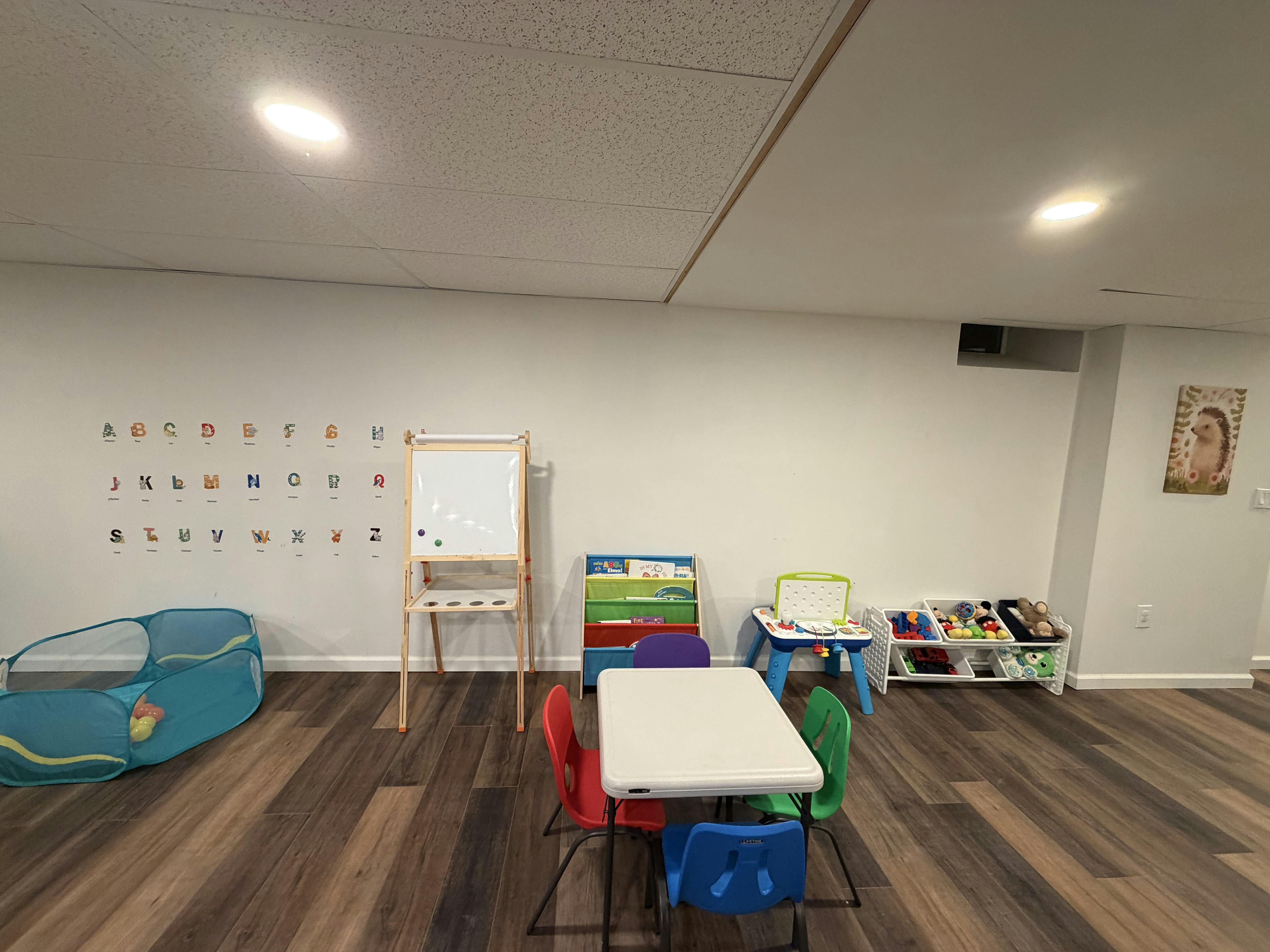Playroom with small table and chairs, whiteboard, alphabet wall decals, and toys