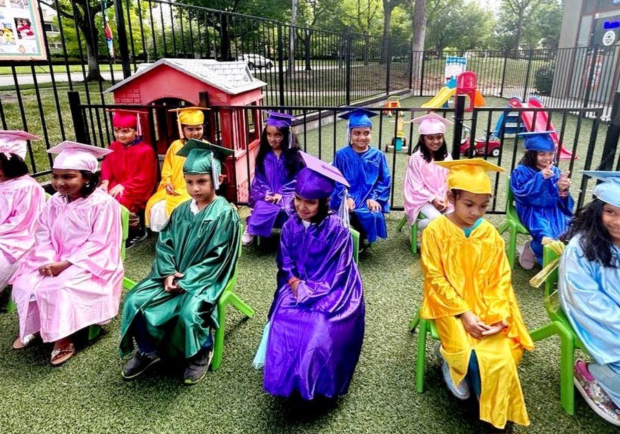 Children in graduation caps and gowns sitting on chairs outdoors