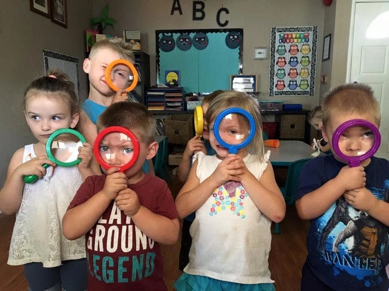 Children holding magnifying glasses up to their faces in a classroom