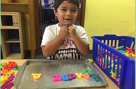 Child playing with colorful letter magnets on a tray