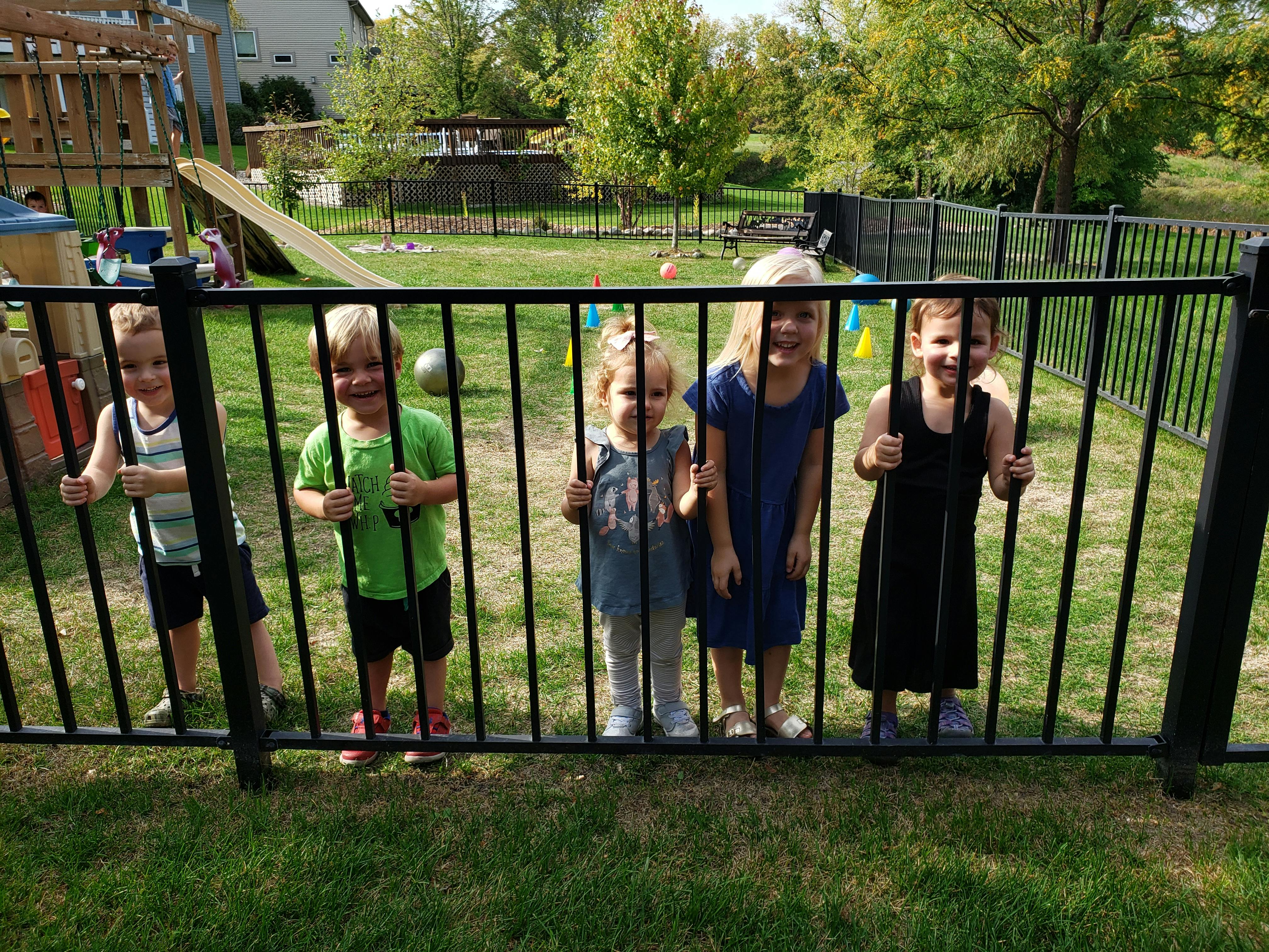 Four children standing behind a black fence on a playground