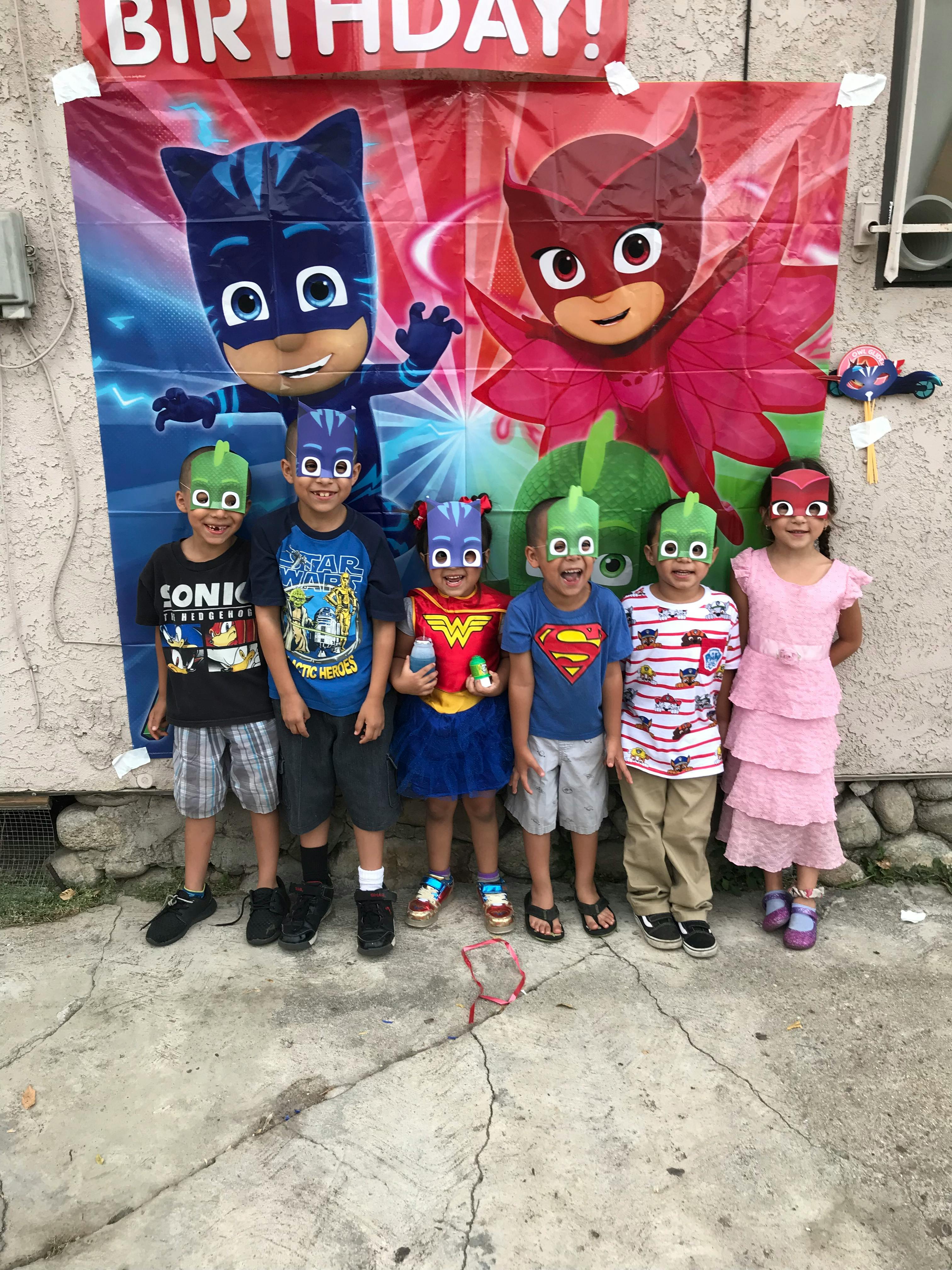 Six children wearing superhero masks standing in front of a birthday banner