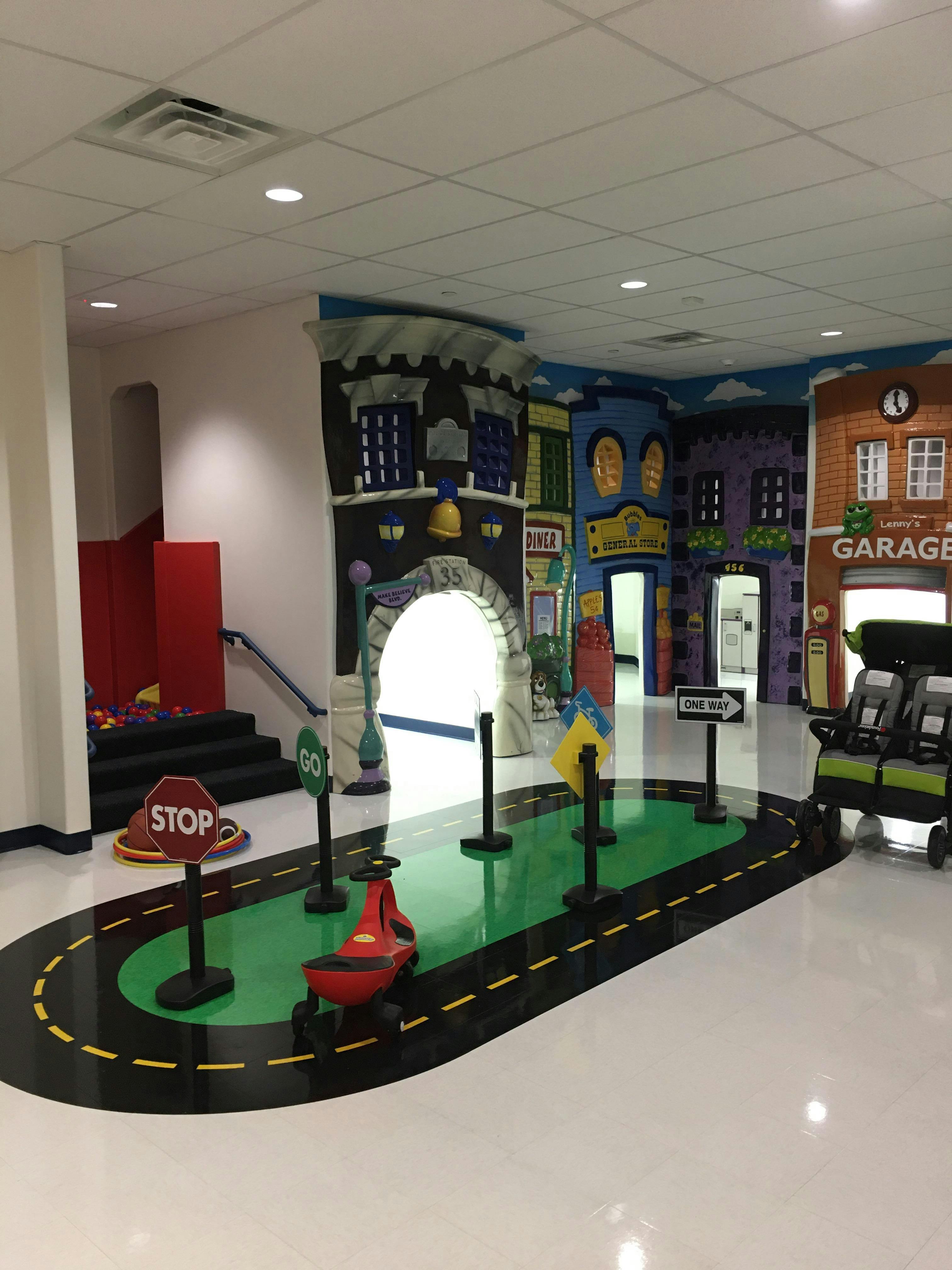 Indoor play area with a road mat, toy car, and building murals