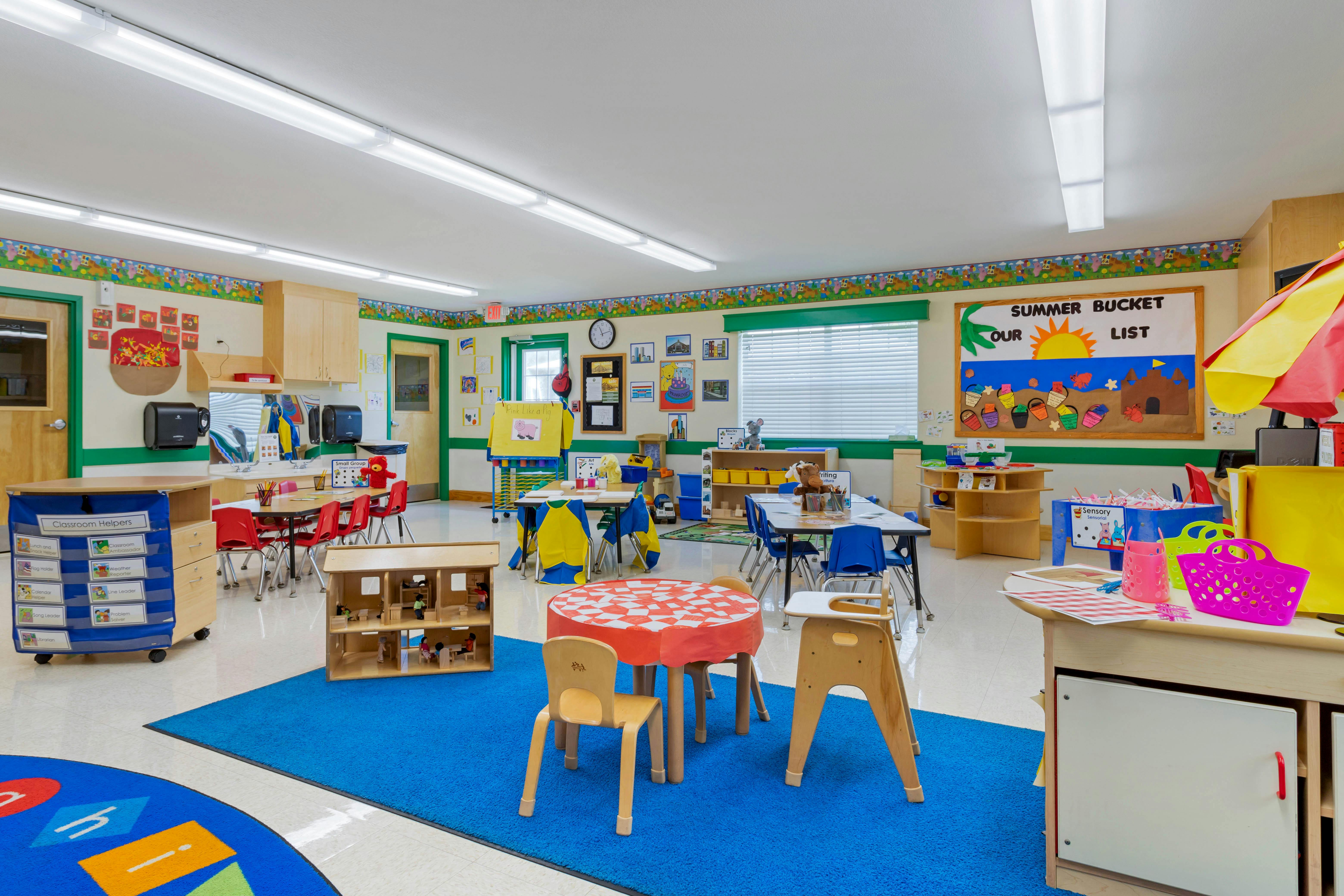 Classroom with tables, chairs, dollhouse, and a "Summer Bucket List" bulletin board