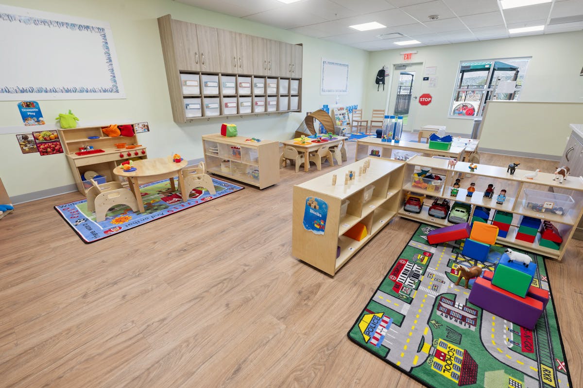 Empty colorful children's classroom with wooden furniture, toys, and activity rugs