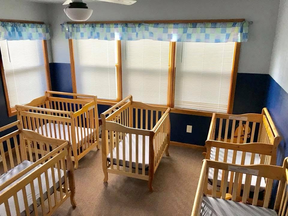 Multiple wooden cribs in a room with windows