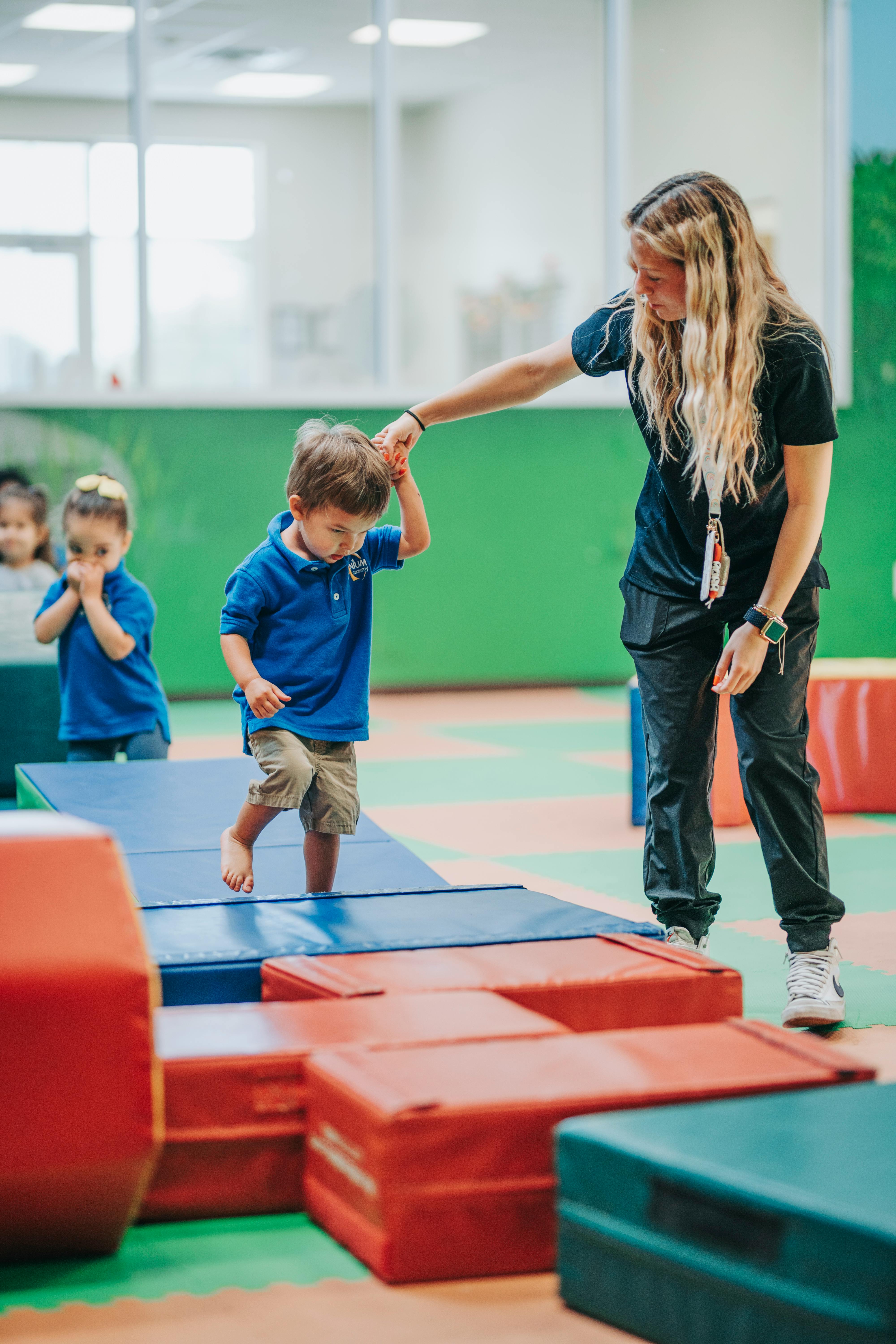 Person helping a child walk on blue and red soft play equipment
