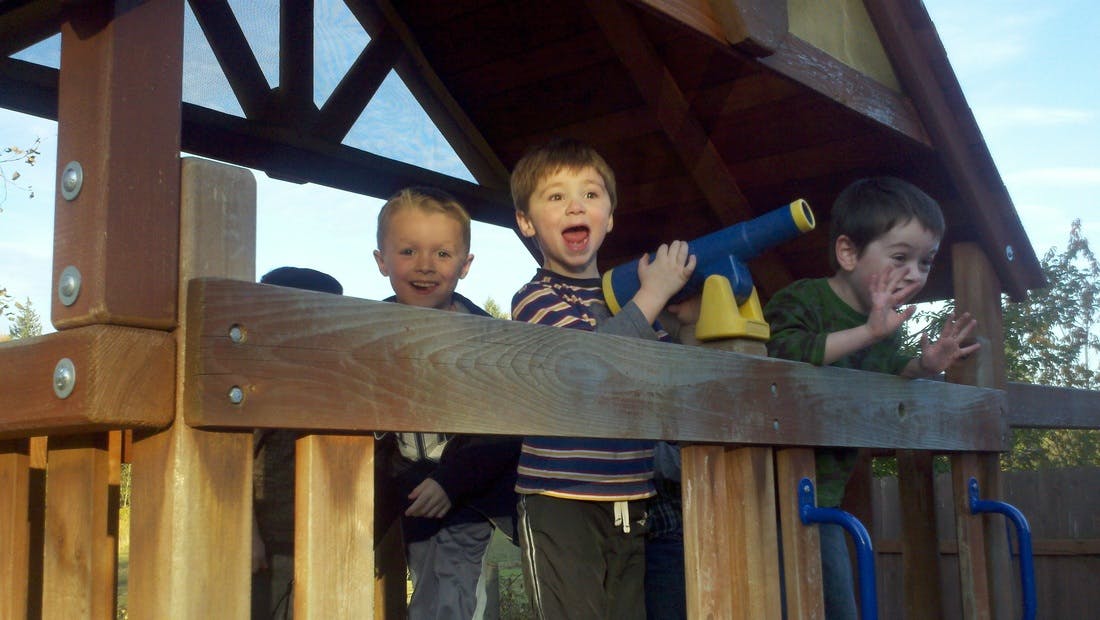 Three children playing on a wooden structure, outdoor play structure