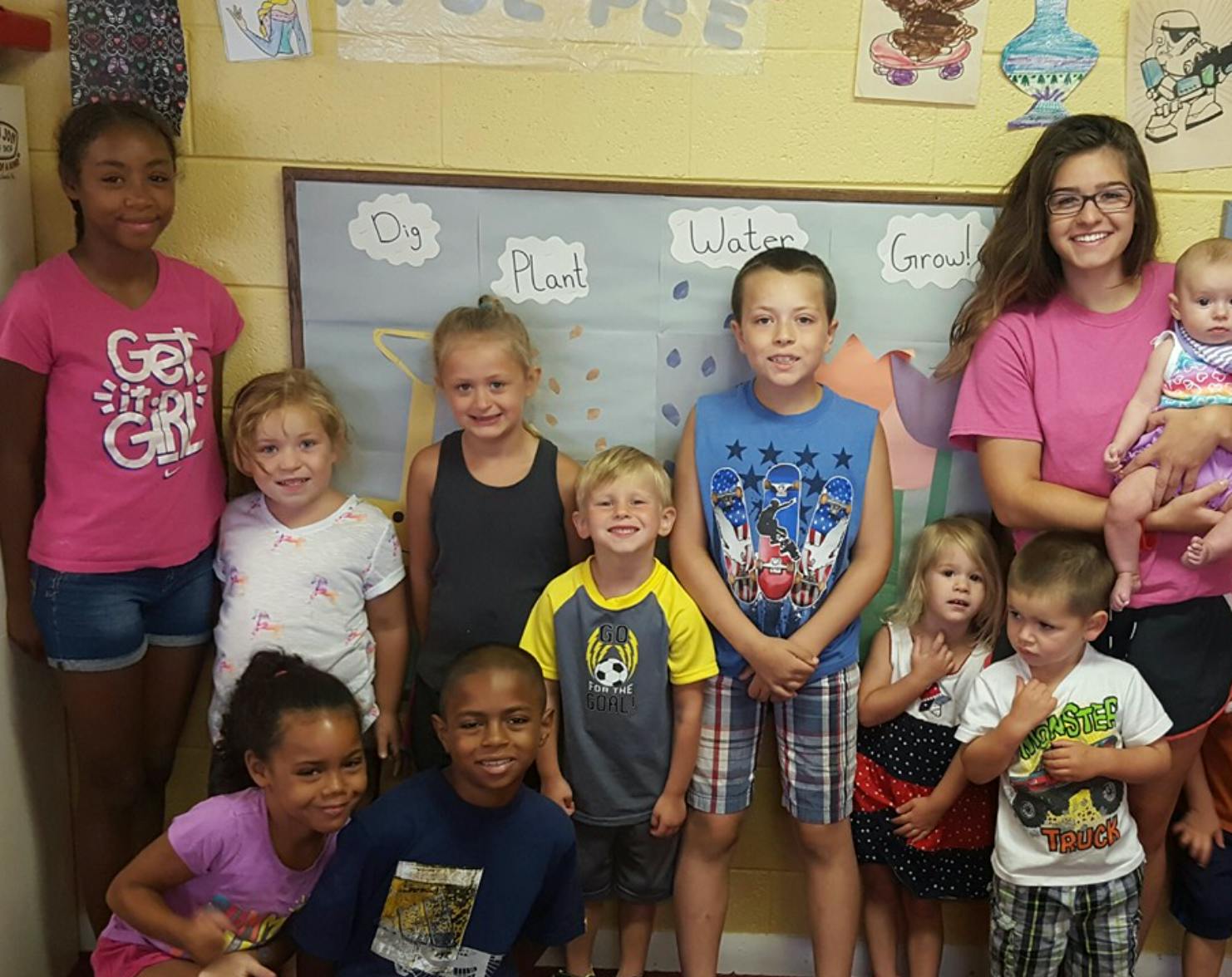 Group of children and adults posing in front of a bulletin board