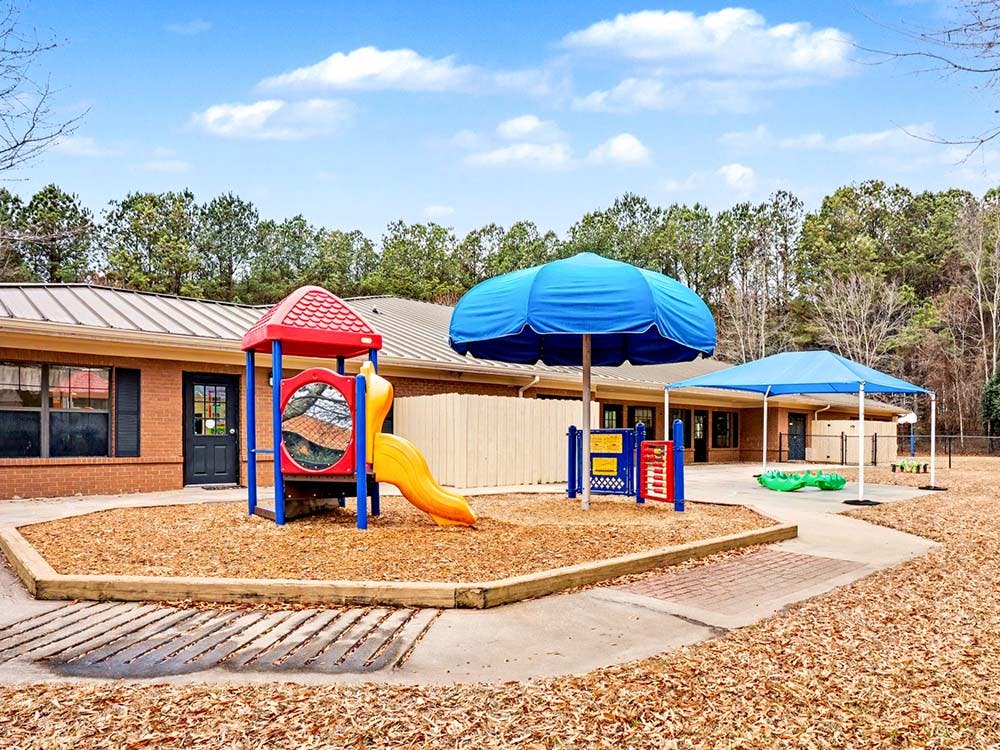 Outdoor playground with a slide and shade structures outside a brick building