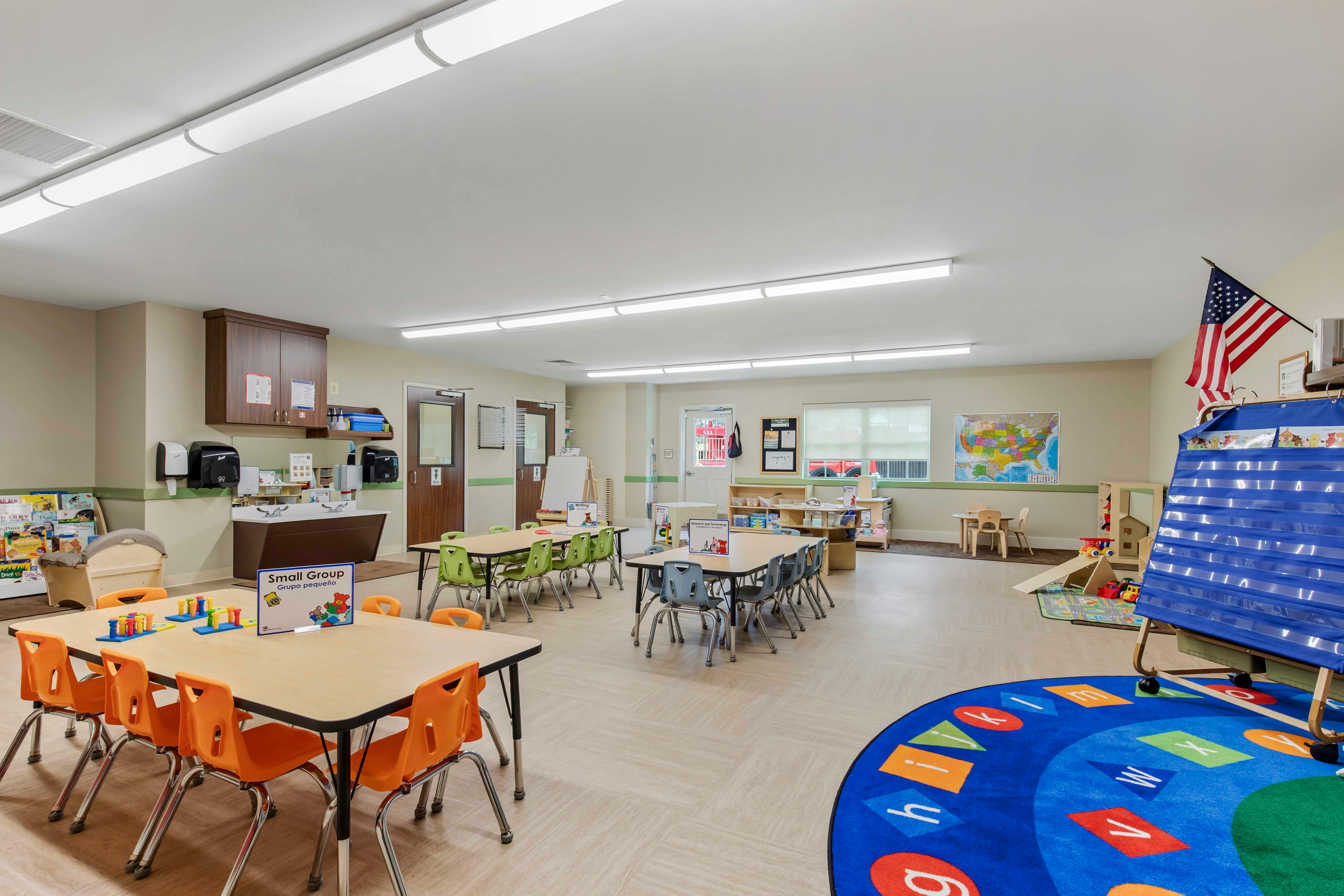 Classroom with child-sized tables and chairs, a map, and an alphabet rug