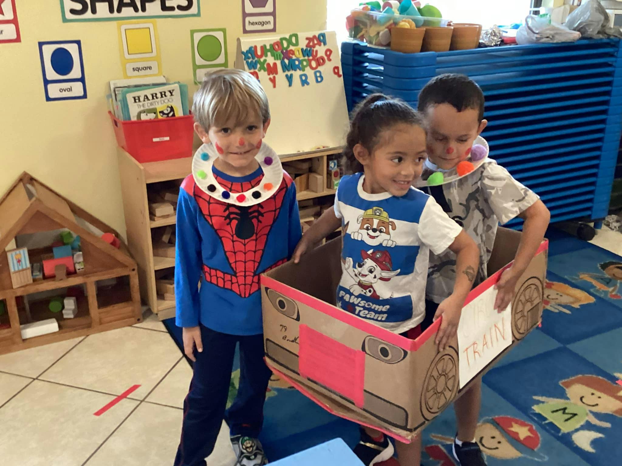 Three children playing with a cardboard box in a classroom