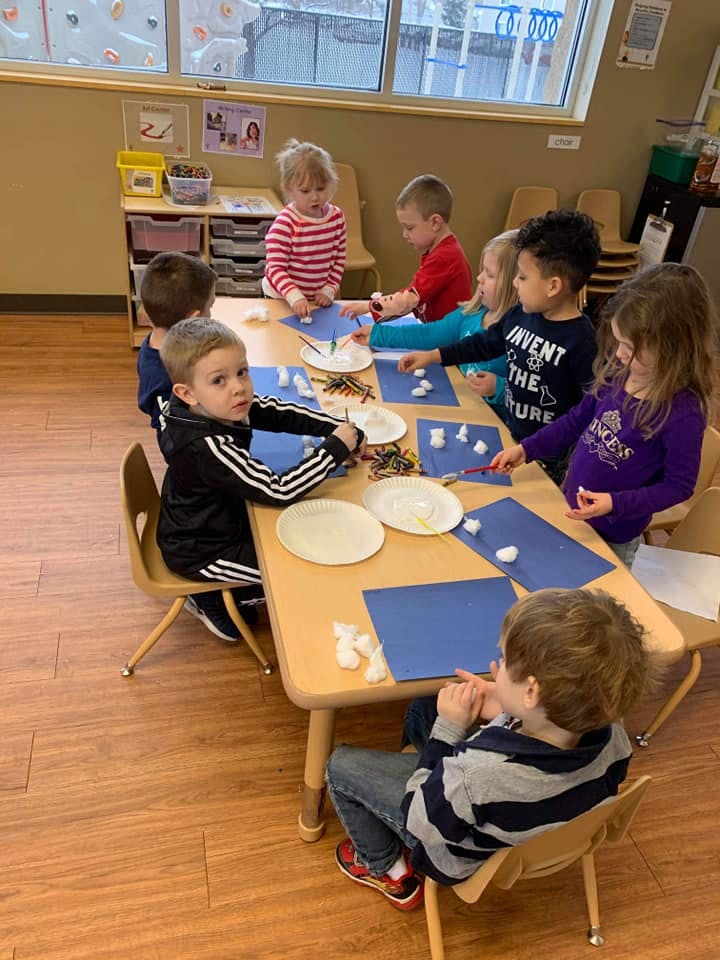 Children at a table doing an art activity with cotton balls and blue paper