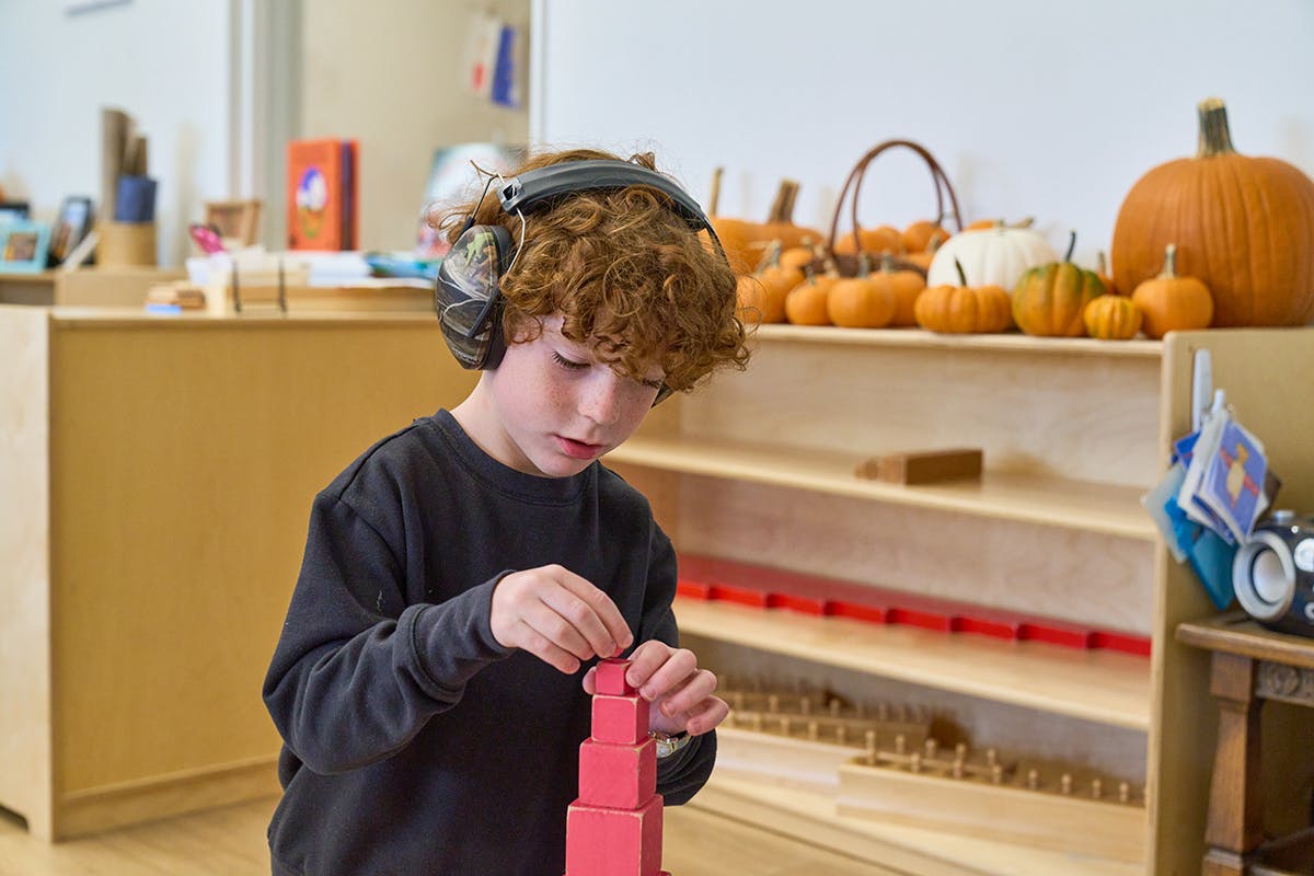Child wearing headphones building with red blocks