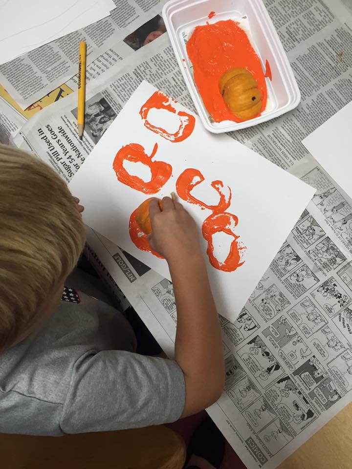 Child making pumpkin prints with orange paint