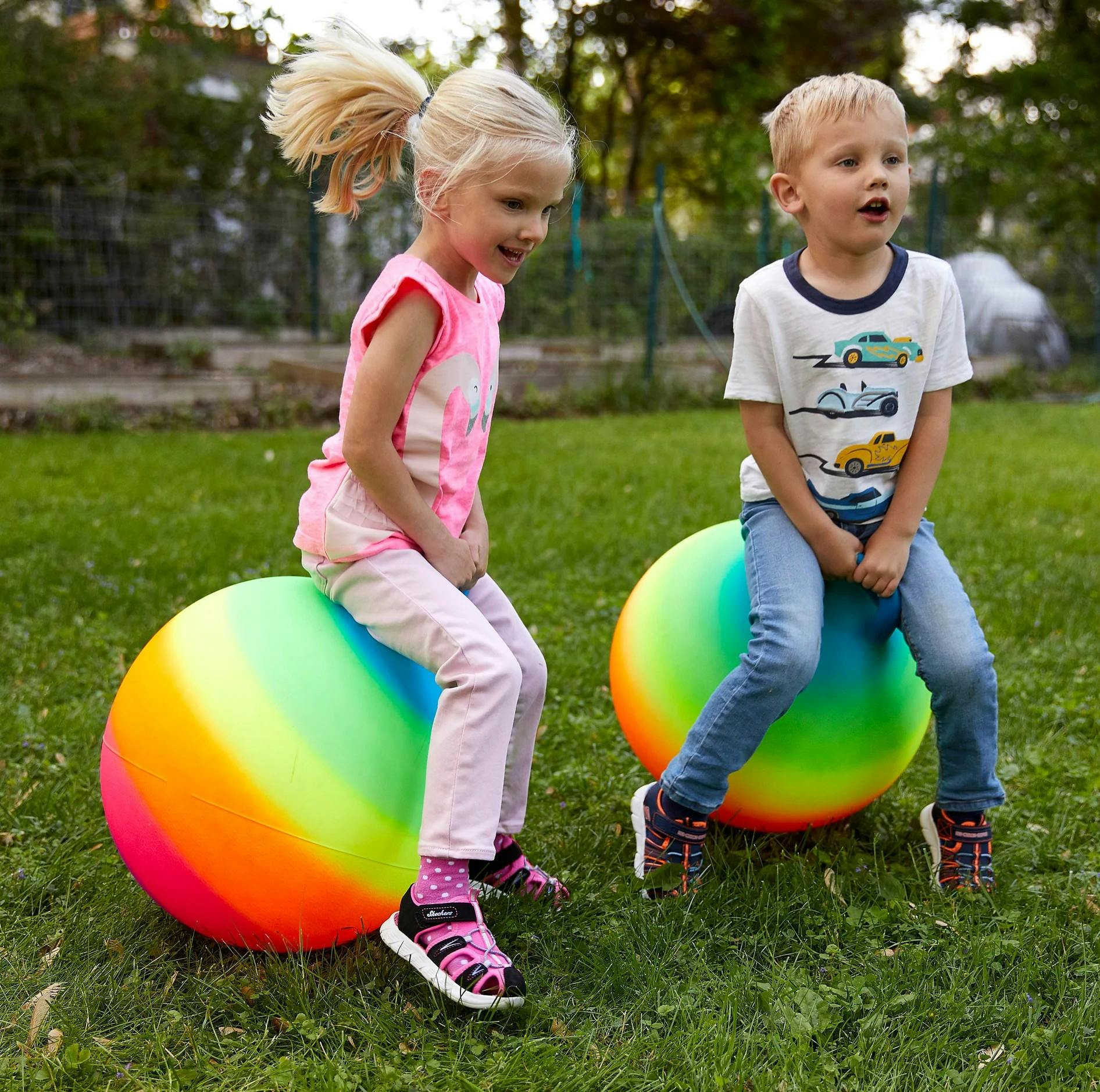 Two children sitting on large colorful balls in grass