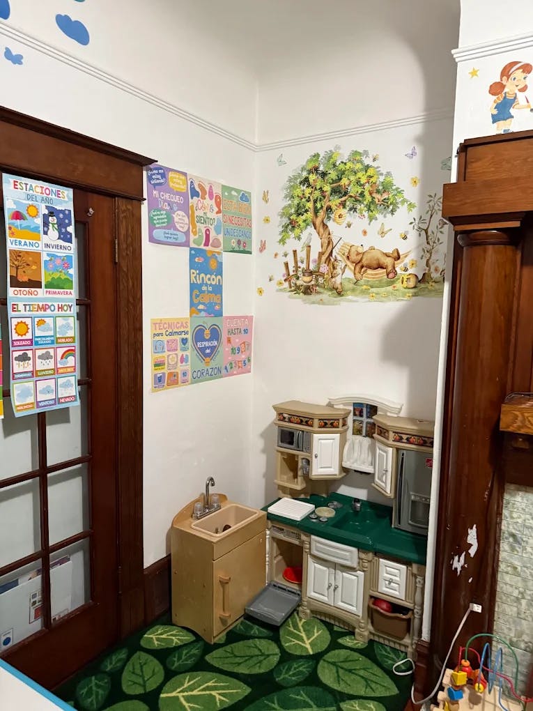 Play kitchen setup in a corner with wall posters and leaf-patterned carpet