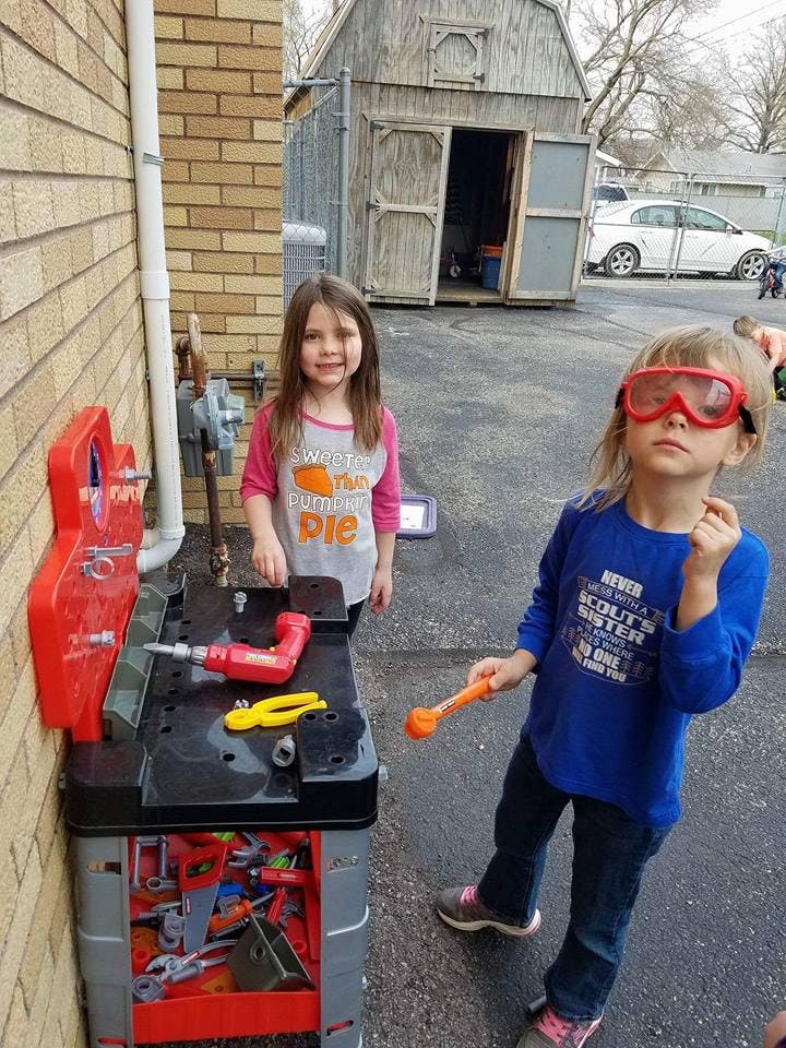 Two children playing with a toy workbench and a toy workbench outdoors