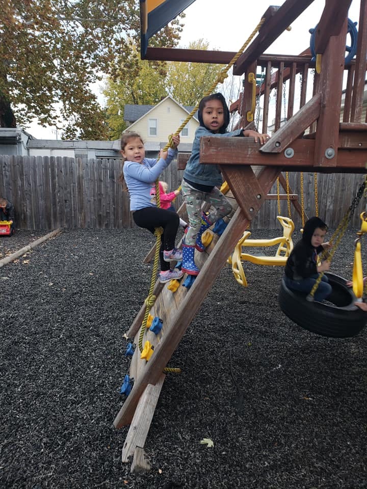 Two children climbing a playset ladder, one child on a tire swing
