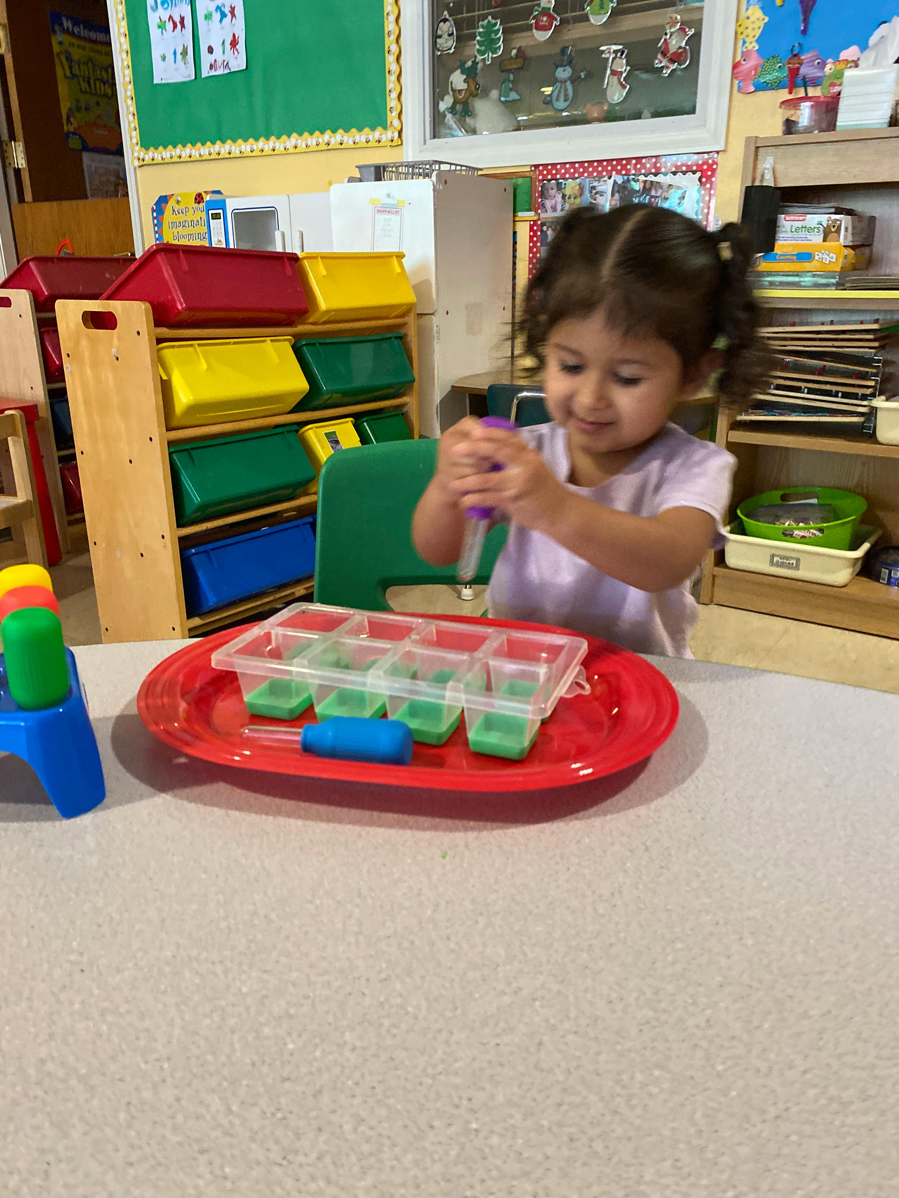 Child playing with a pipette and a tray of plastic compartments in a classroom