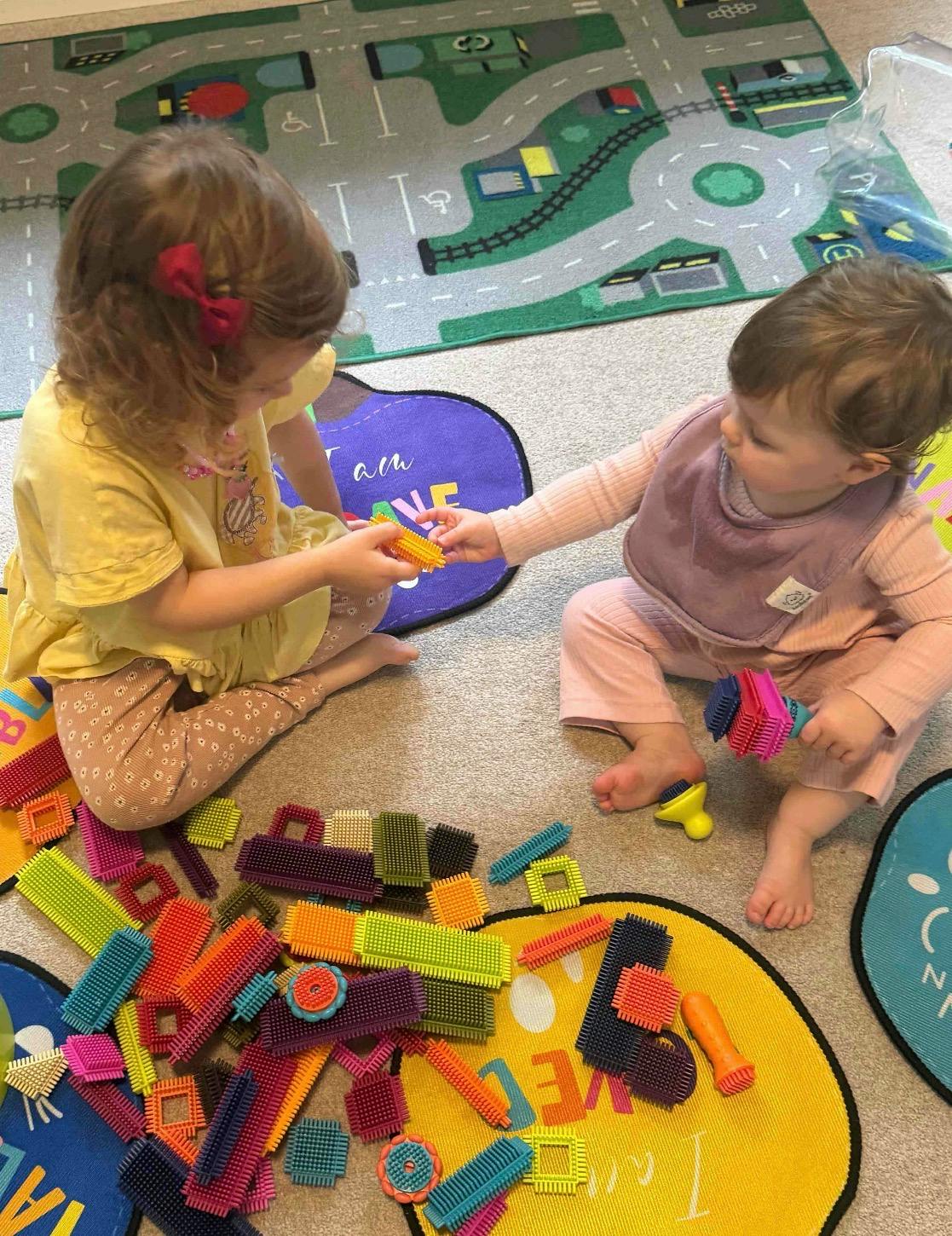 Two children sitting on a play rug building with colorful plastic sensory blocks