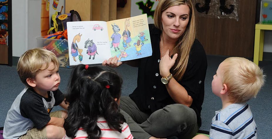 Person reading a book to three children in a classroom