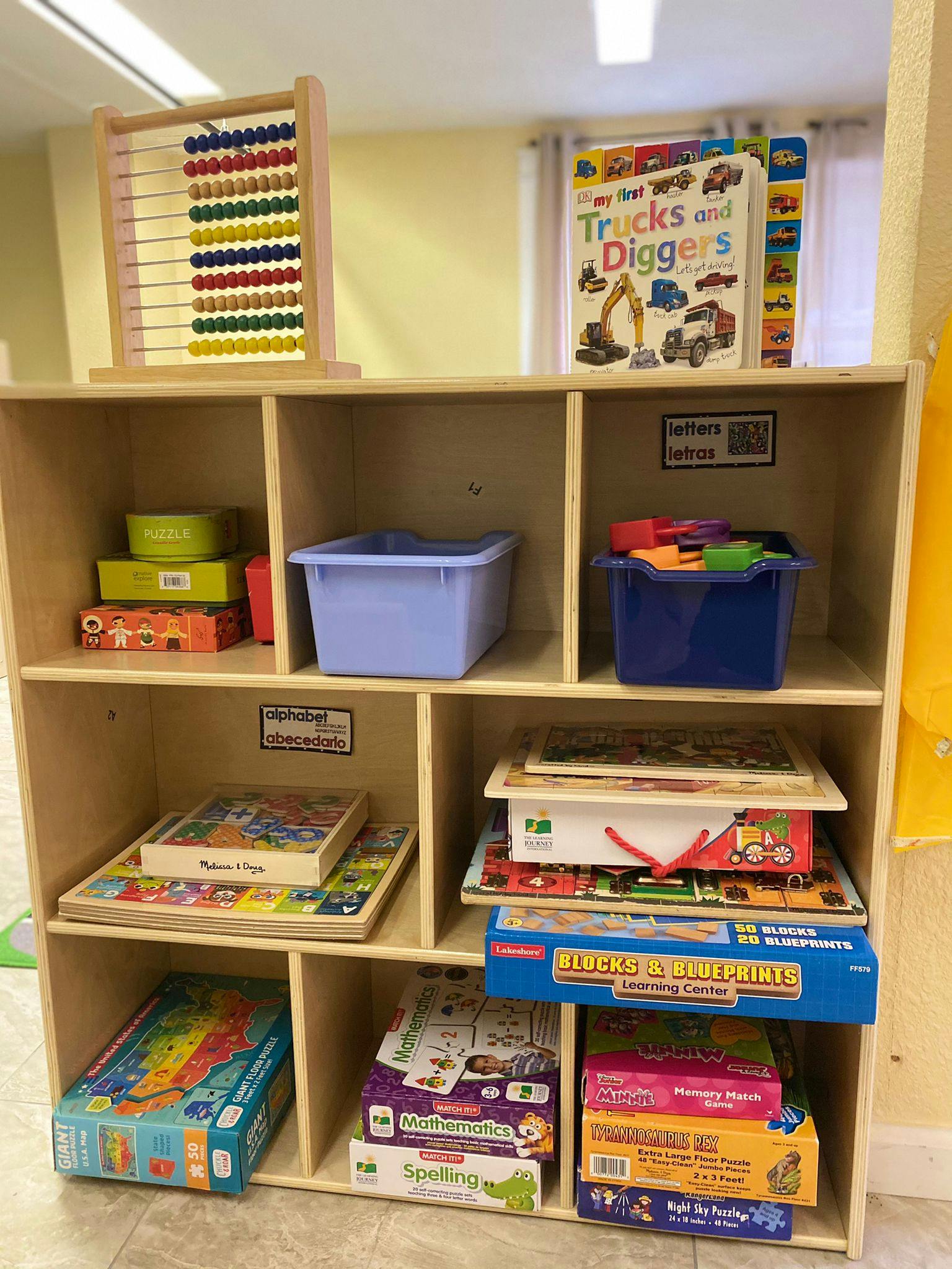 Wooden shelf unit filled with puzzles, toys, and books, including an abacus on top