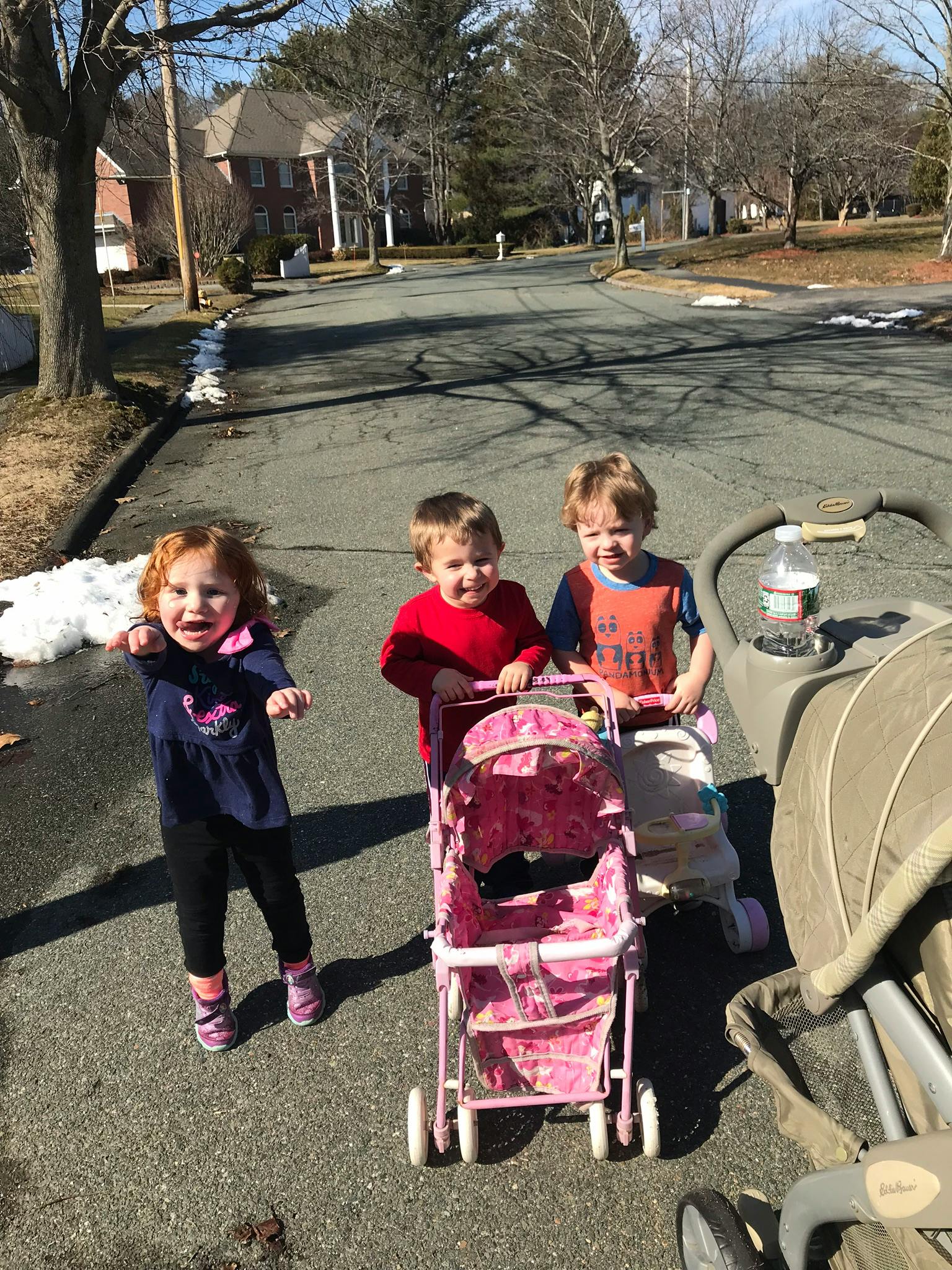 Three children on a paved surface, two pushing strollers