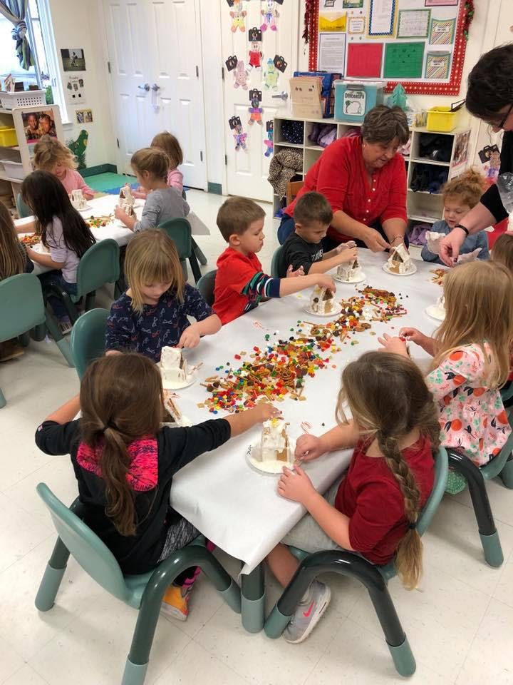 Adult and children decorating gingerbread houses at a table
