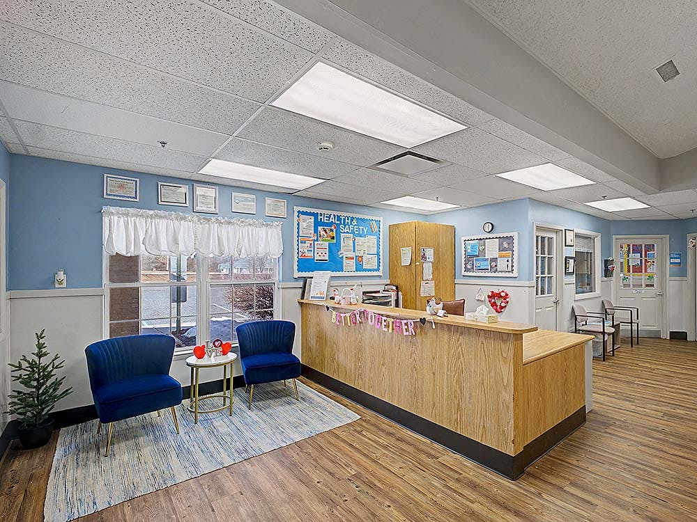 Reception area with wooden desk, two blue chairs, and a window