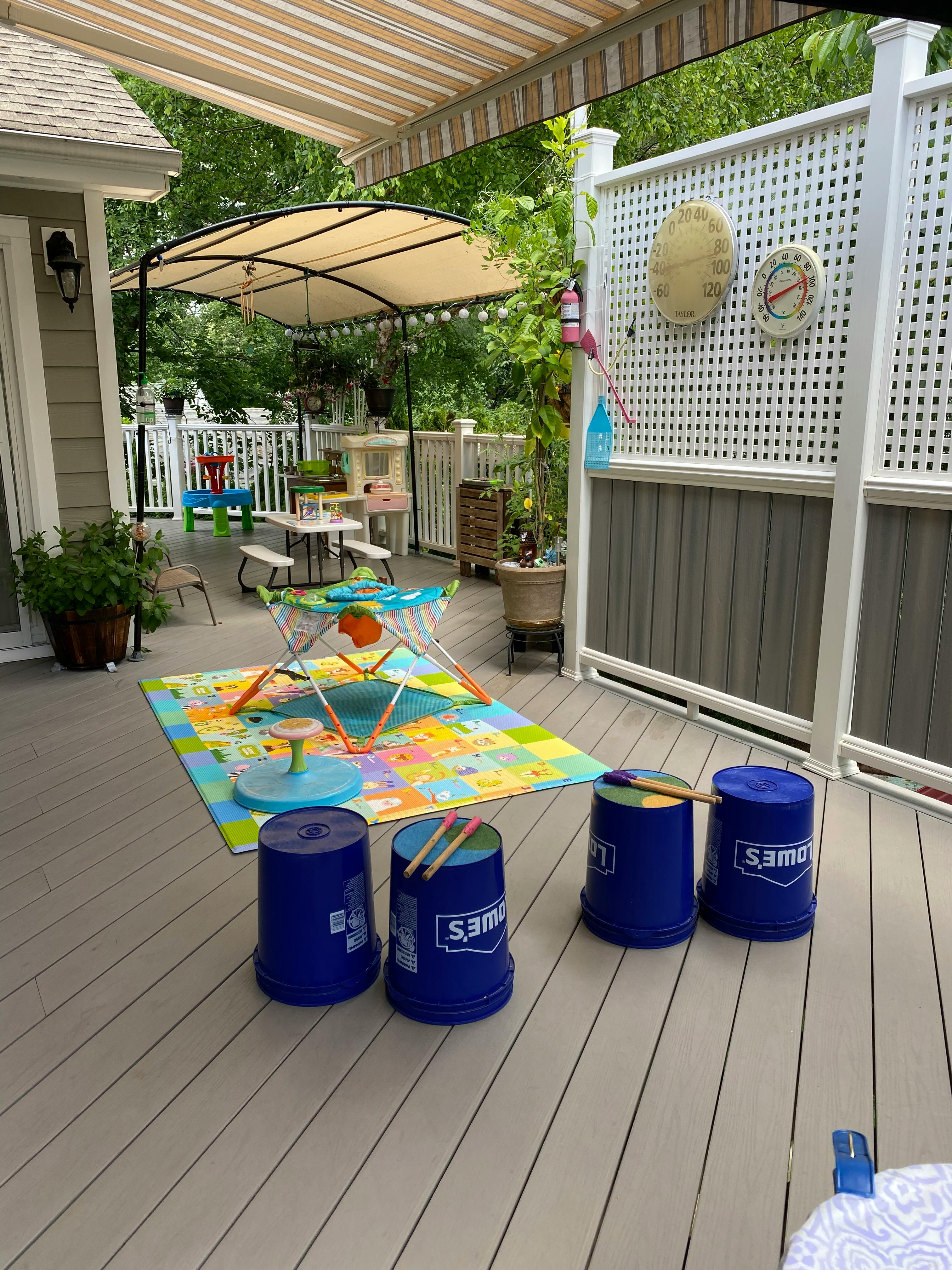 Outdoor deck with play area, colorful mat, and blue buckets