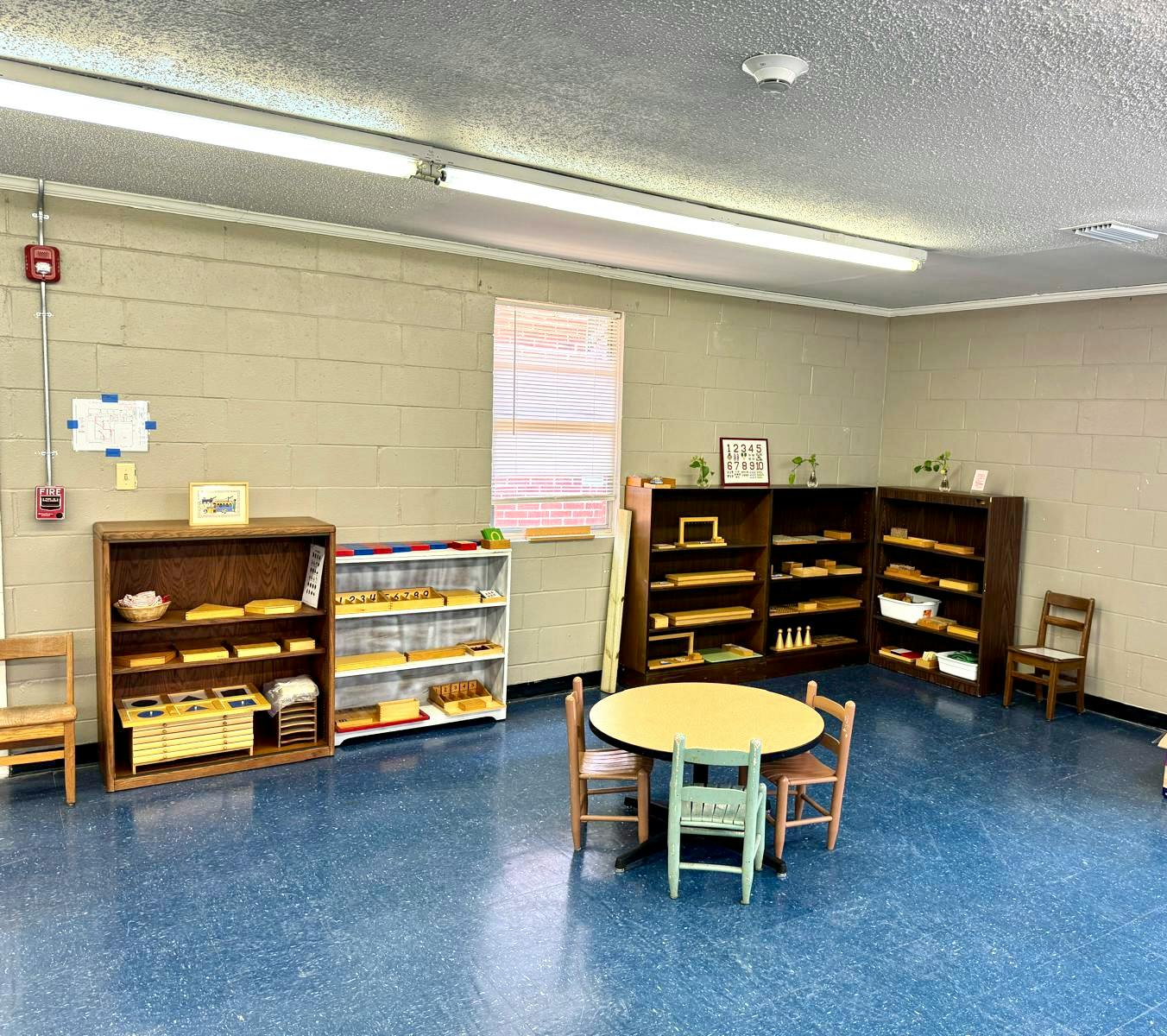 Classroom with small tables and chairs, shelves with learning materials