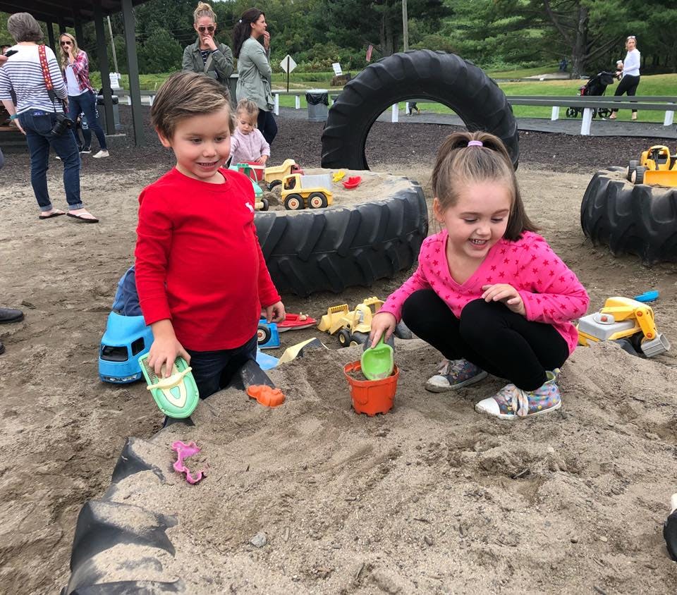 Two children playing in a sandbox with toys