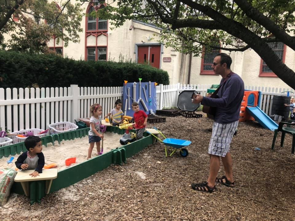 Person playing guitar for children in a sandbox