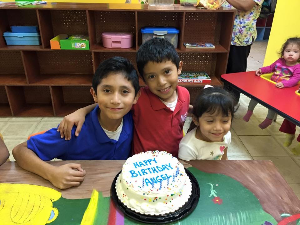 Three children and a birthday cake with "Happy Birthday Angel" written on it