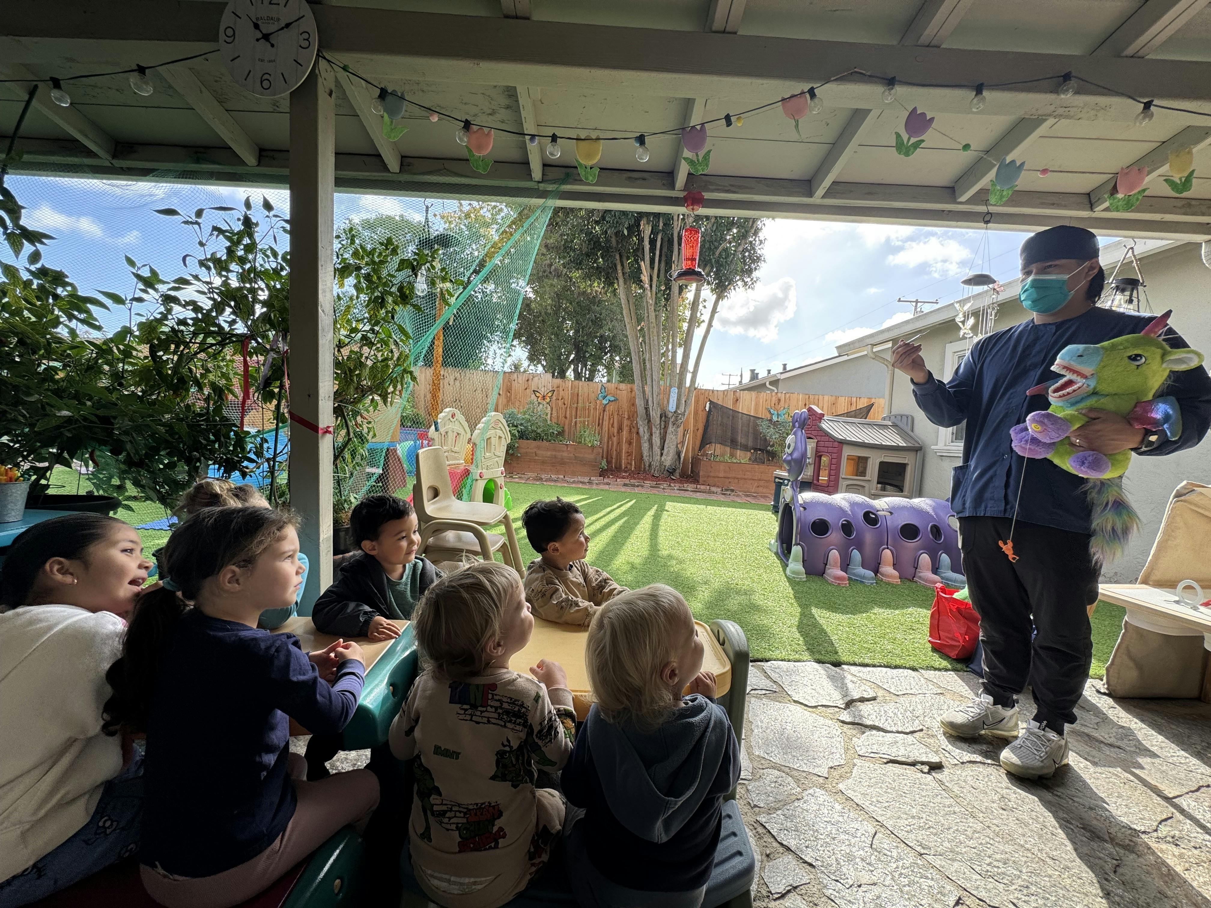 Person in mask holding a stuffed animal and speaking to children