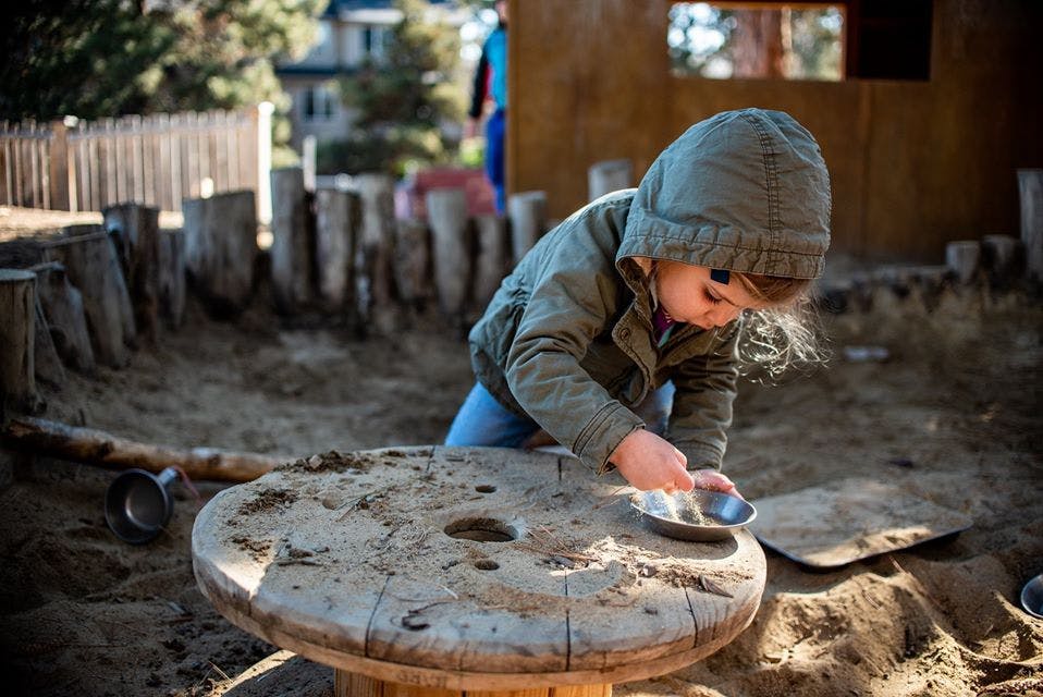 Child playing with a small dish on a wooden spool in a sandbox