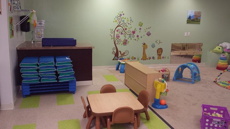 Children's play area with small tables and chairs, toys, and wall decals
