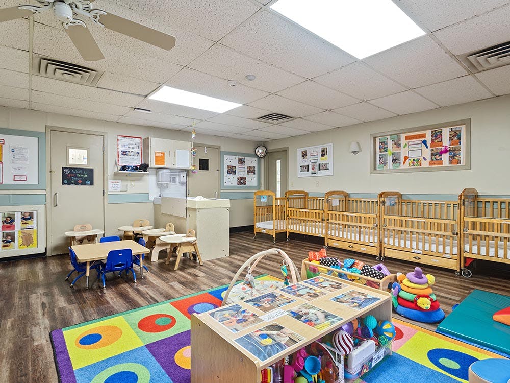 Classroom for young children with cribs, small tables, and play area