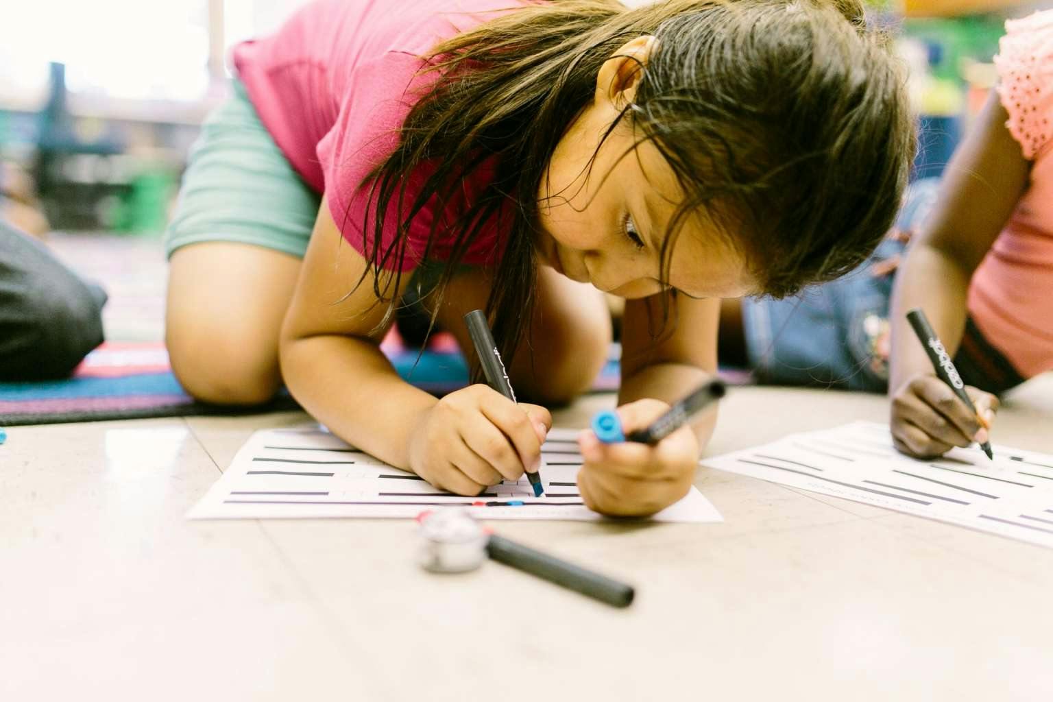 Child kneeling and writing on paper with a marker