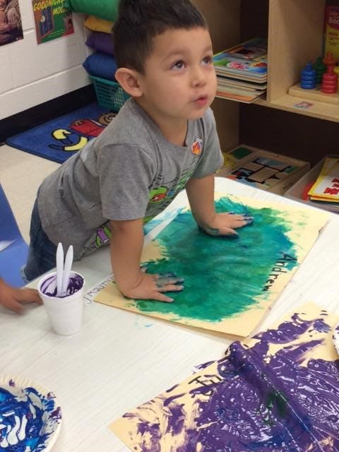 Child with hands in green paint on paper