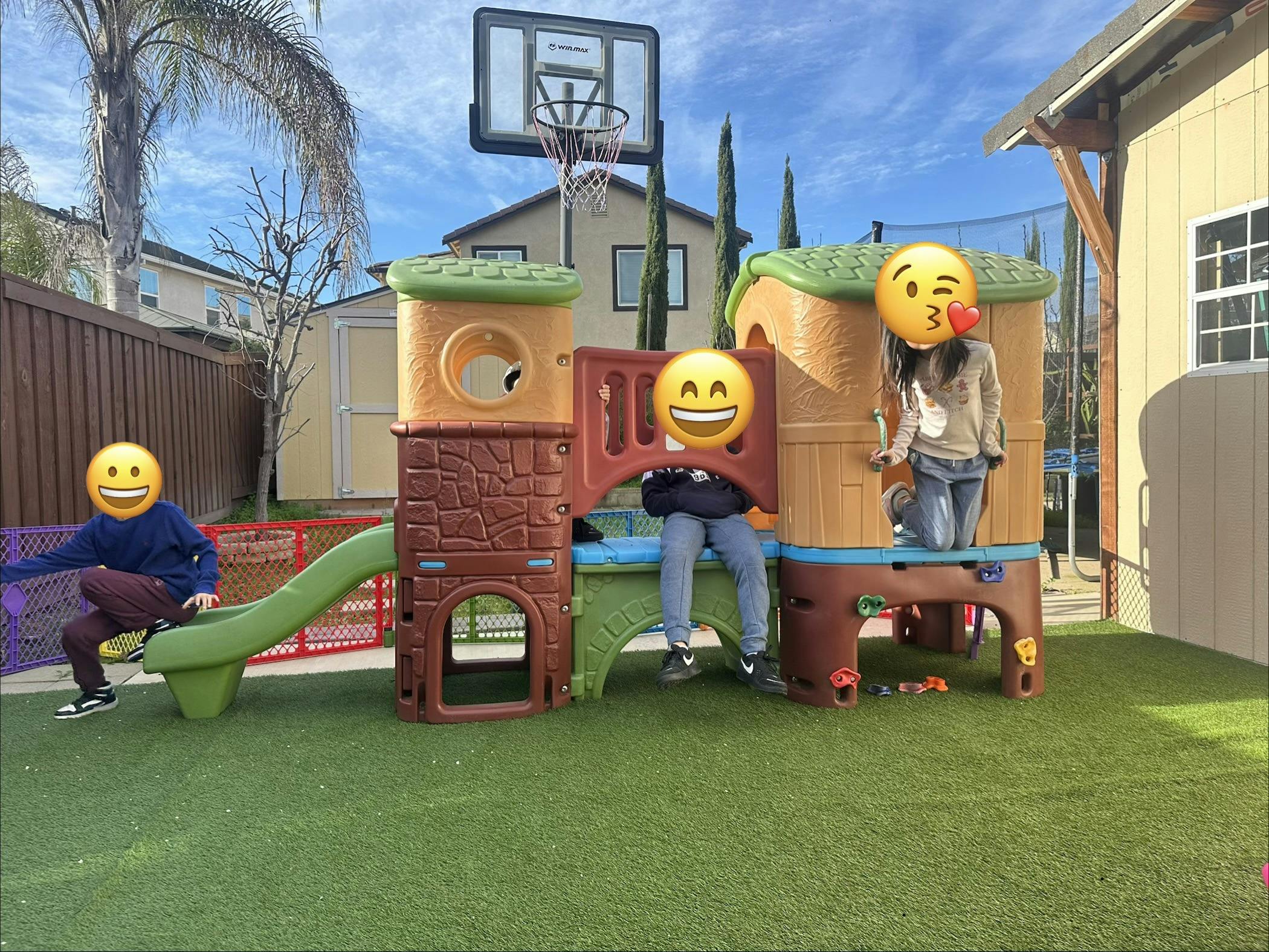 Three children playing on a colorful playground set with a slide