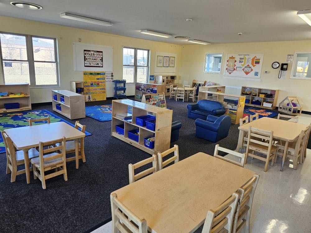 An empty early childhood classroom with small tables, chairs, and shelves