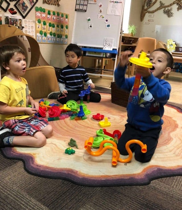 Three children playing with toys on a rug in a classroom