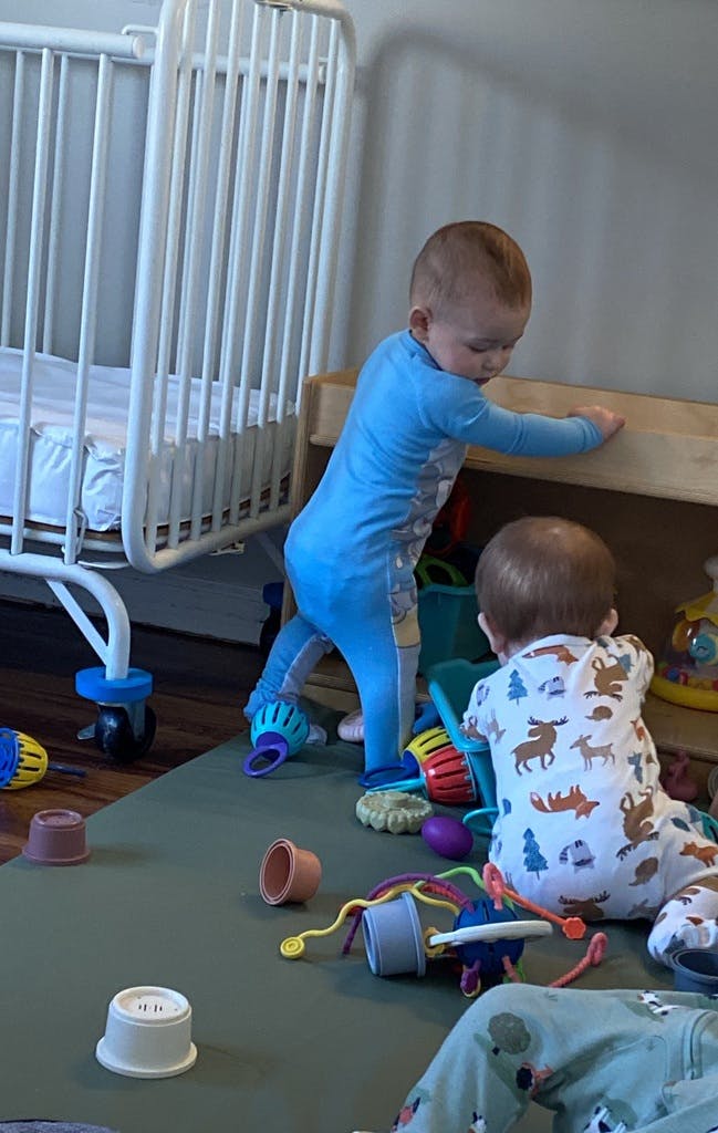 Two children playing with toys on a mat next to a crib