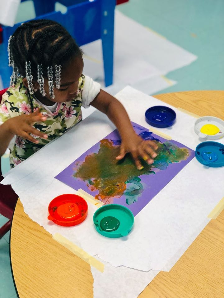 Child finger painting on purple paper at a table